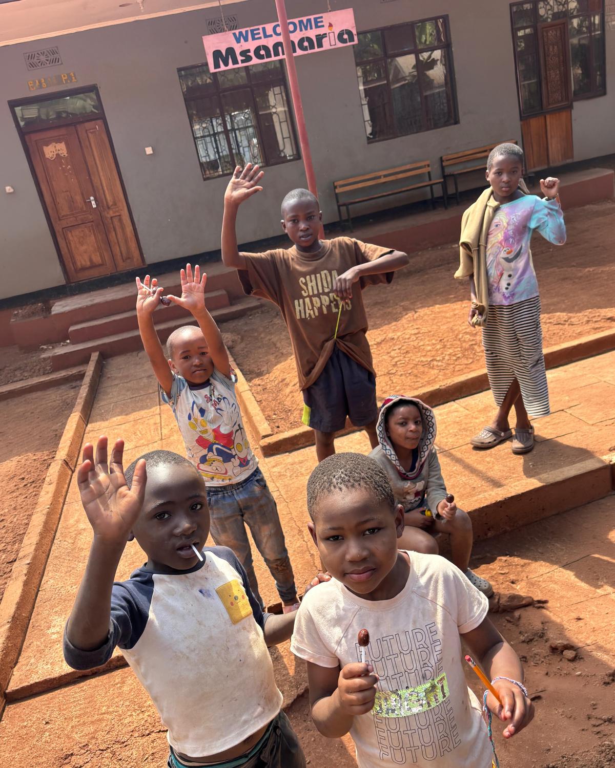 Un grupo de niños del orfanato de Moshi saluda a cámara en el patio de la escuela.