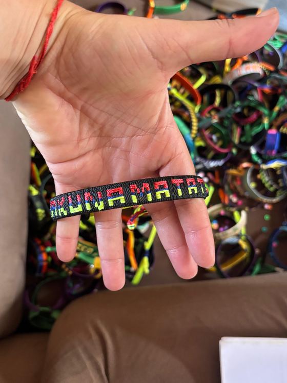 Una mano sostiene una pulsera tejida a mano sobre una caja llena de pulseras de colores.